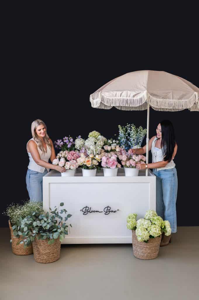 Elegant floral arrangement at XO Flowers floral booth with two women arranging flowers.