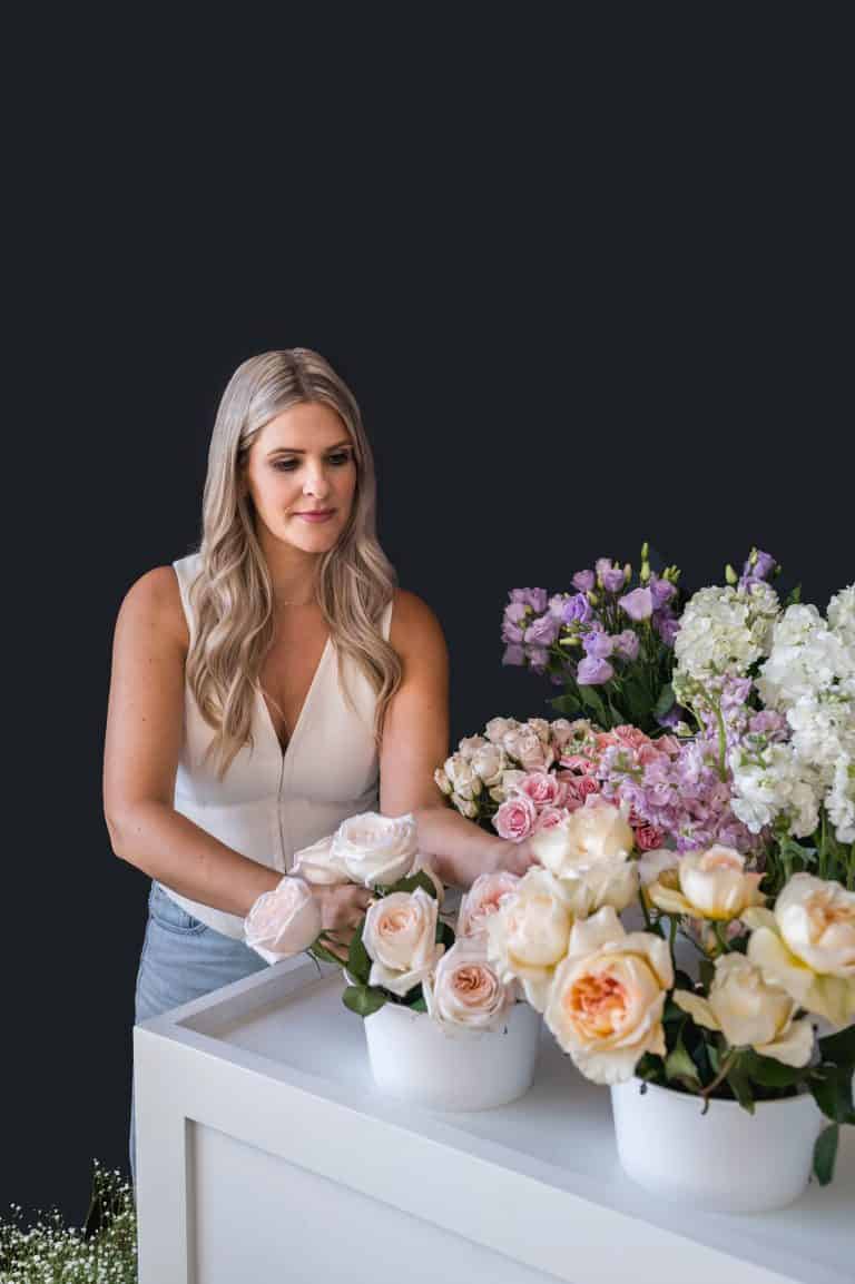 Woman arranging beautiful pastel-colored roses and peonies for event decor.