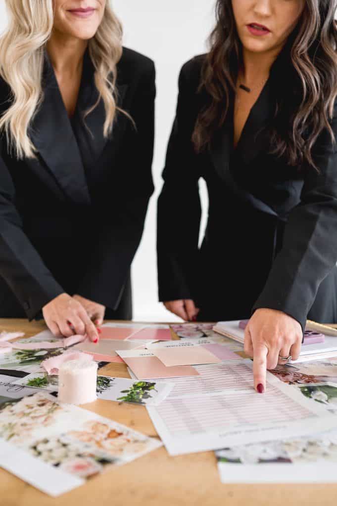 Two women in black blazers discussing floral arrangements at a table.