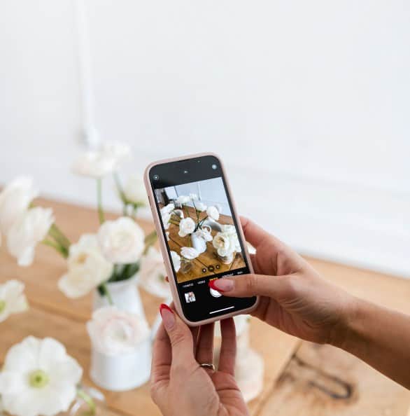 Person taking photo of white floral arrangements with smartphone.