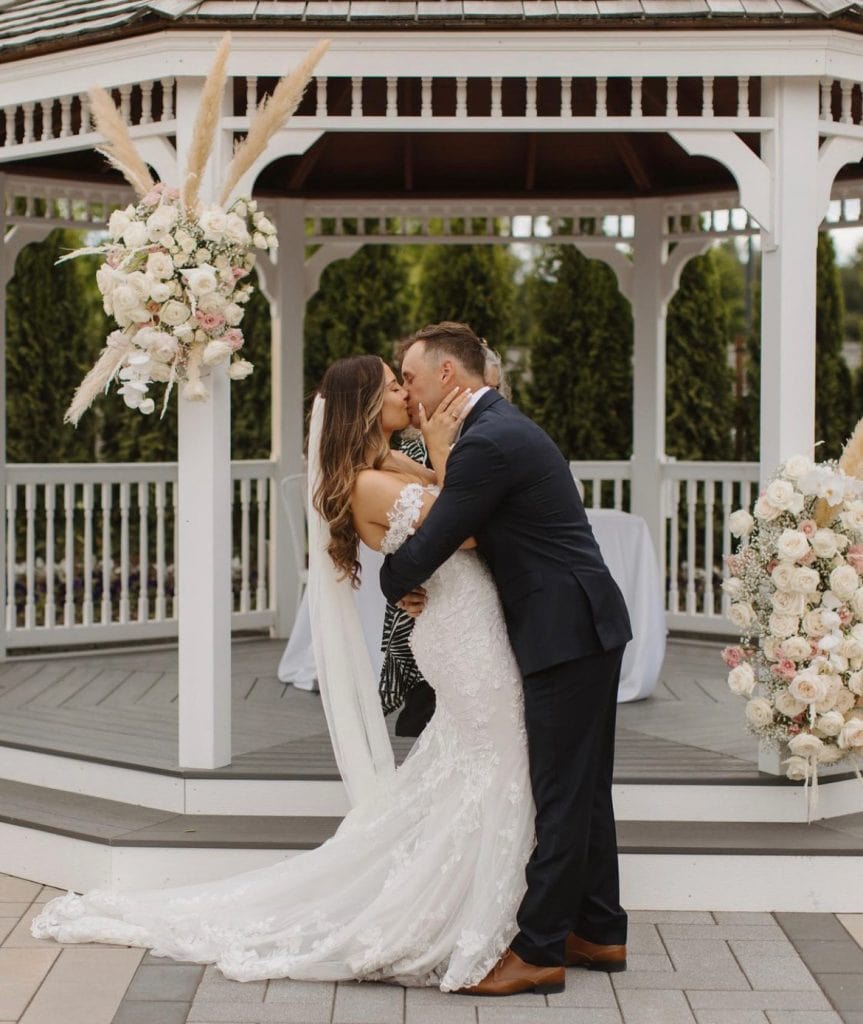 Bride and groom kissing under a floral gazebo with elegant wedding flowers.