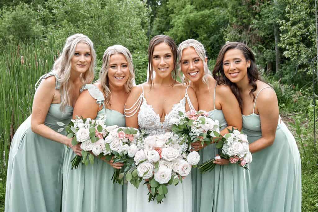 Bridal party with floral bouquets outdoors, wedding celebration, elegant dresses, natural setting.