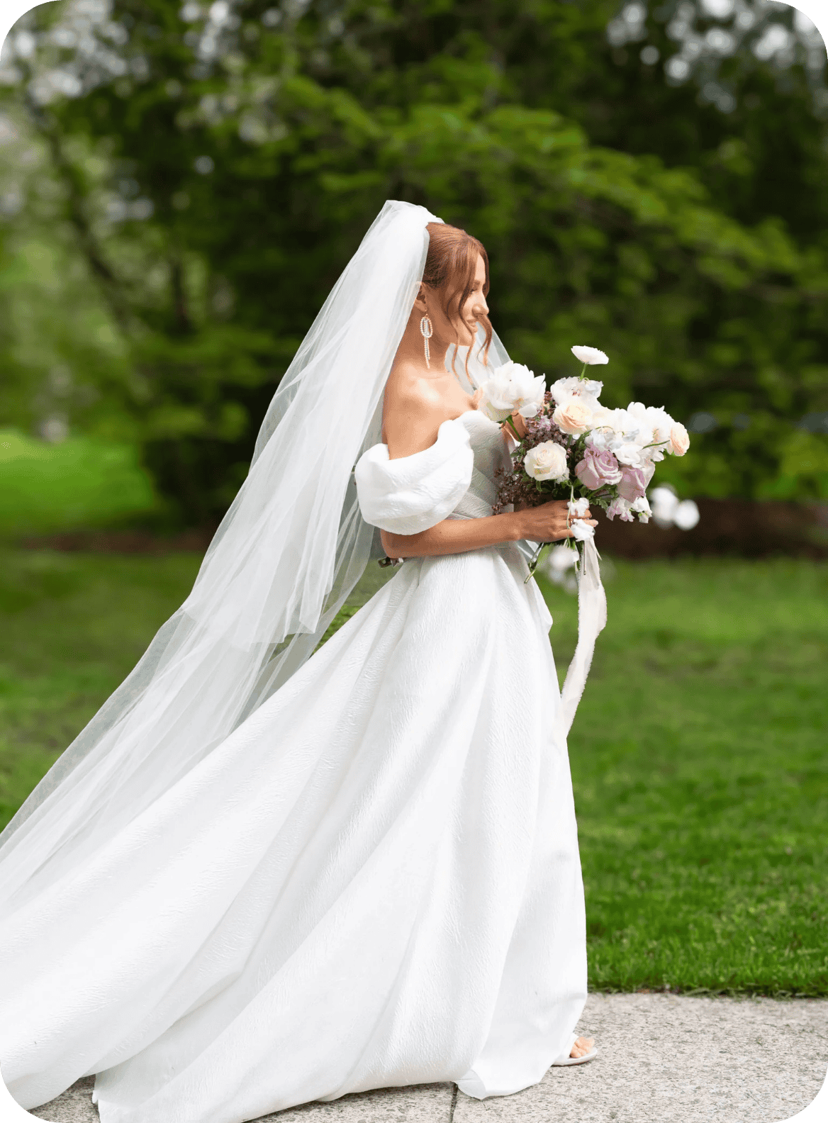 Bride in white wedding dress holding a floral bouquet outdoors.