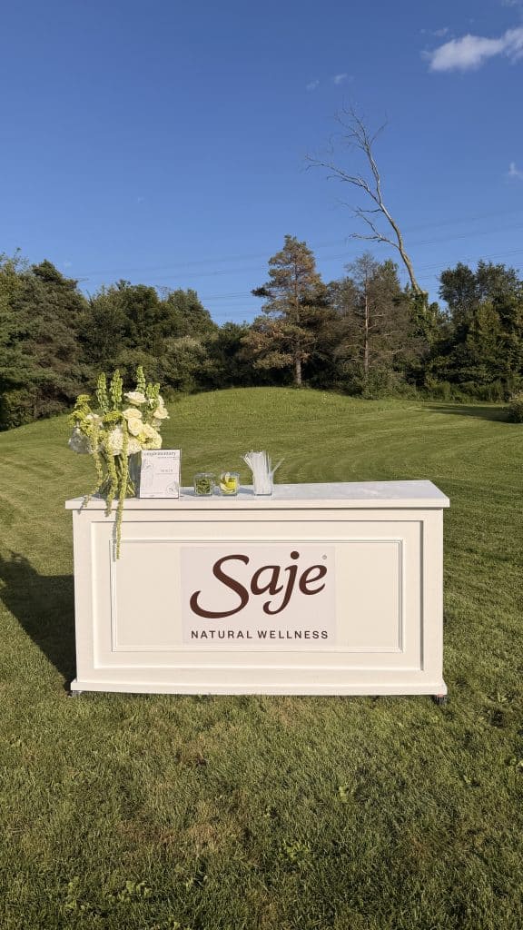 Elegant outdoor event bar with floral decor and Saje Natural Wellness branding.
