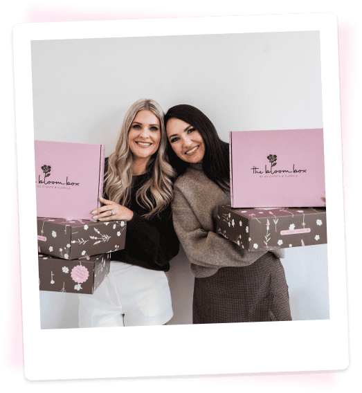 Two women holding pink floral gift boxes smiling at the camera.