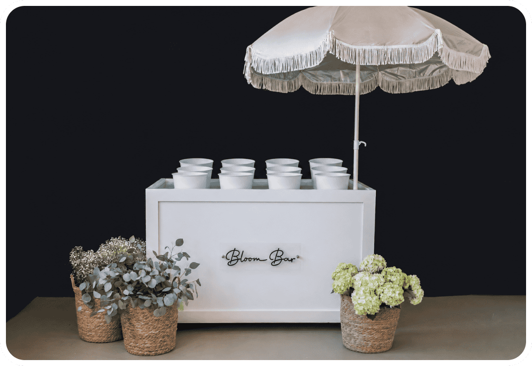 Bloom Bar with floral arrangements and white cups under a large umbrella.