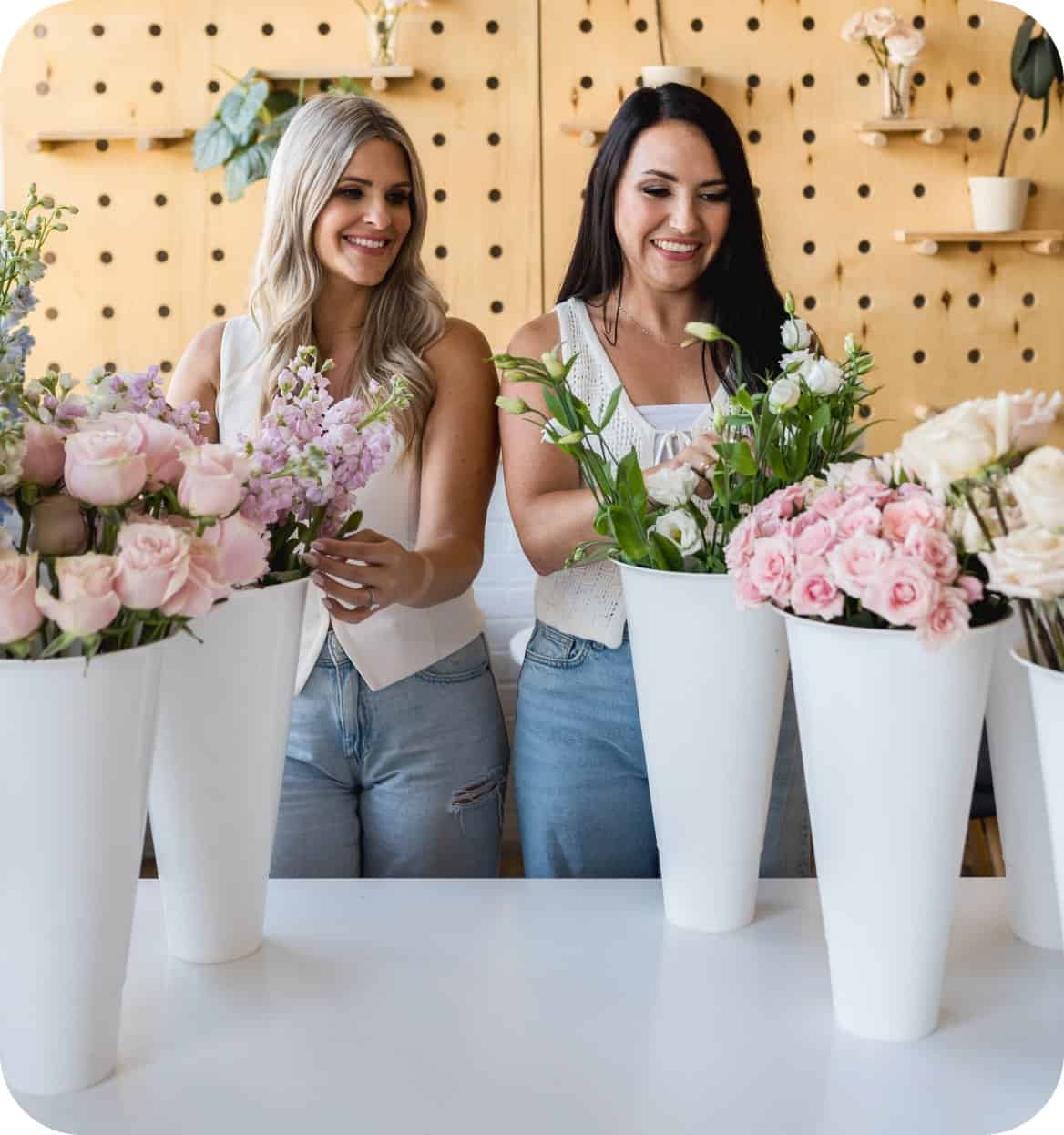 Two women arranging pink and white floral bouquets at XO Flowers.