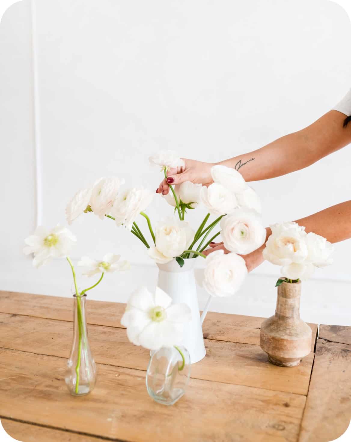 Beautiful white flower bouquet in a white vase with a person's hands arranging flowers.