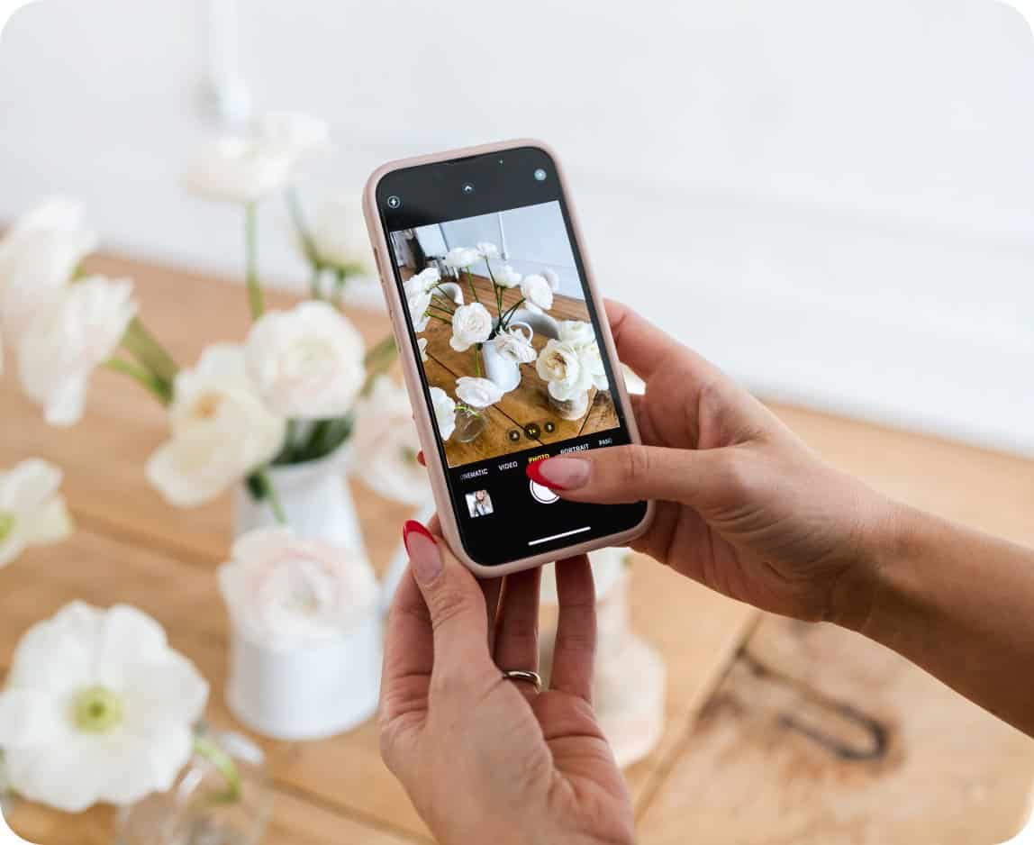 Person taking a photo of white floral arrangements with a smartphone.